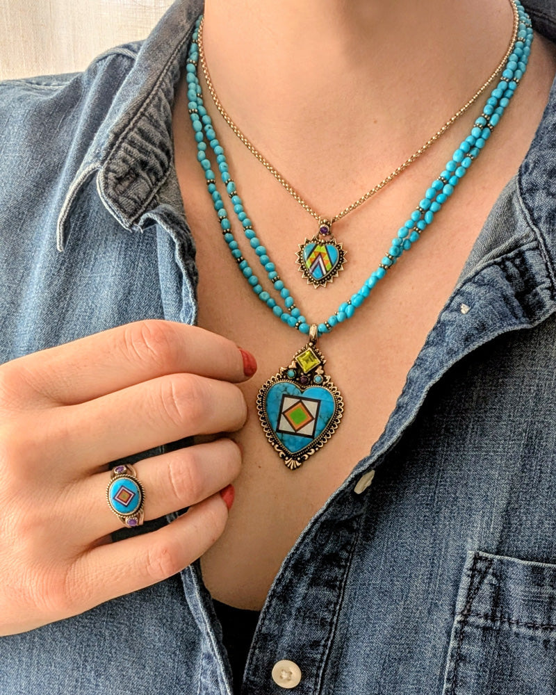 turquoise beaded necklace with turquoise heart inlay by aldrich art jewelry  worn by a woman with a brown leather hat on